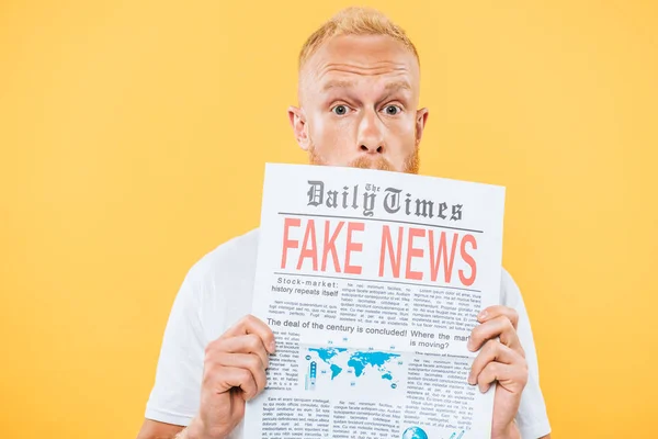 Surprised bearded man holding newspaper with fake news, isolated on yellow — Stock Photo