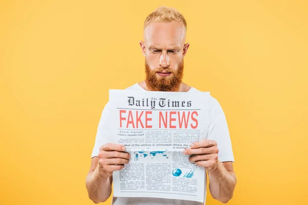 Hombre barbudo serio leyendo el periódico con noticias falsas, aislado en amarillo - foto de stock