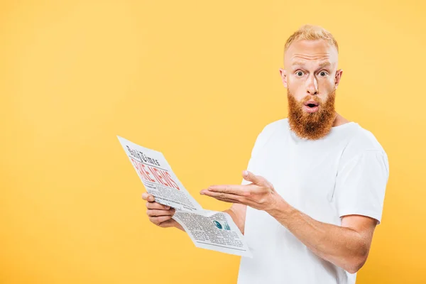 Surprised man showing newspaper with fake news, isolated on yellow — Stock Photo