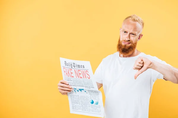 Bärtiger Mann hält Zeitung mit Fake News in der Hand und zeigt Daumen nach unten, isoliert auf gelb — Stockfoto