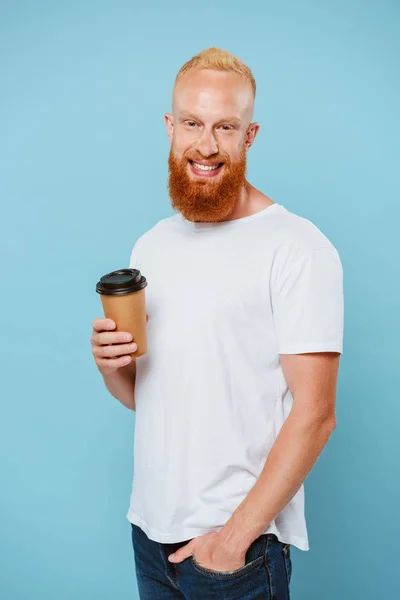 Uomo barbuto sorridente in t-shirt che tiene il caffè per andare, isolato su blu — Foto stock