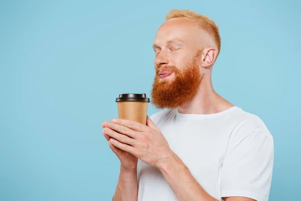 Smiling bearded man in t-shirt holding coffee to go with closed eyes, isolated on blue — Stock Photo
