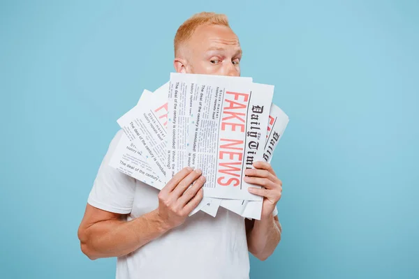 Ängstlicher gutaussehender Mann, der Zeitungen mit Fake News hält, isoliert auf blauem Grund — Stockfoto