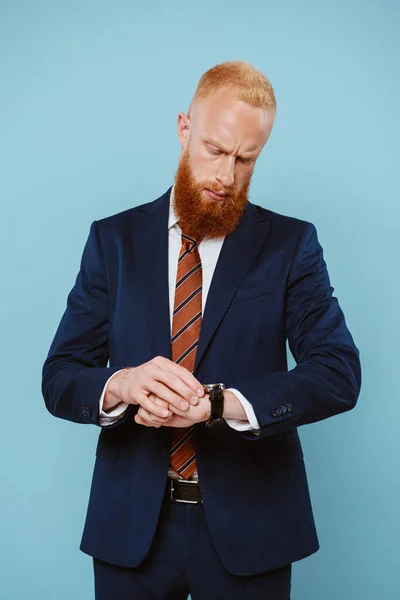 Homem de negócios barbudo pensivo em terno olhando para relógio, isolado em azul — Fotografia de Stock