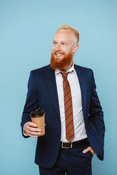 Счастливый красивый бизнесмен в костюме, держащий кофе, чтобы пойти, изолированный на голубом — стоковое фото