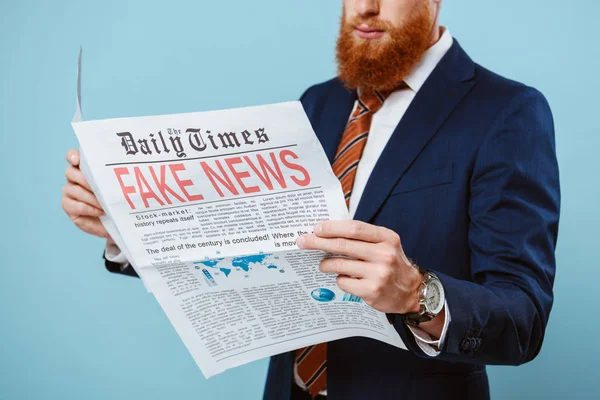 Cropped view of businessman reading newspaper with fake news, isolated on blue — Stock Photo
