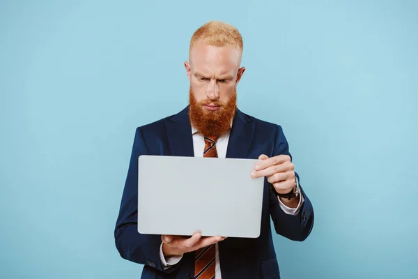 Sérieux homme d'affaires barbu en costume à l'aide d'un ordinateur portable, isolé sur bleu — Photo de stock