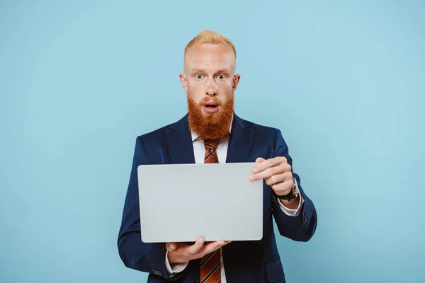 Schockierter bärtiger Geschäftsmann im Anzug mit Laptop, isoliert auf blauem Grund — Stockfoto