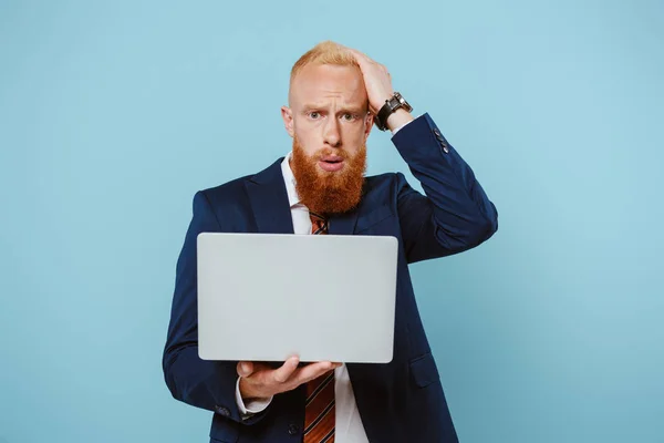 Preoccupato uomo d'affari barbuto in giacca e cravatta con computer portatile, isolato su blu — Foto stock