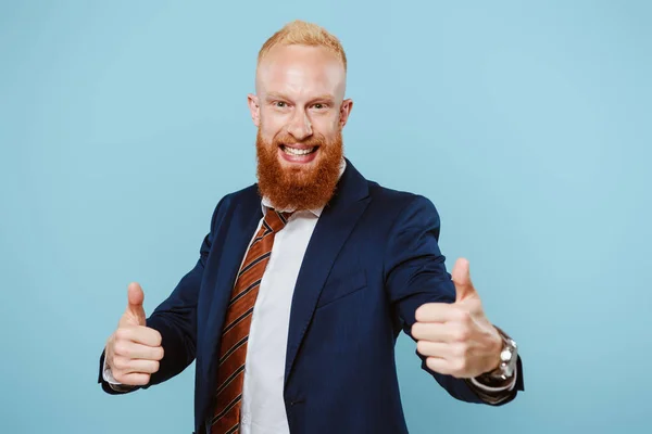 Hombre de negocios barbudo excitado en traje mostrando pulgares hacia arriba, aislado en azul - foto de stock