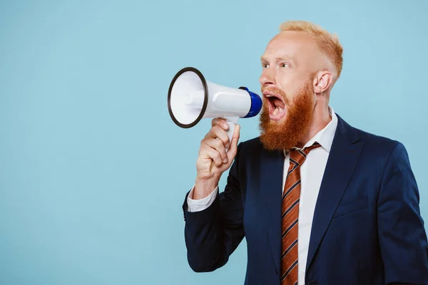 Angry bearded businessman shouting into megaphone, isolated on blue — Stock Photo