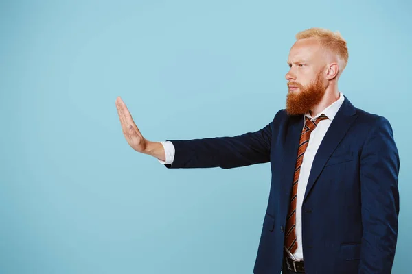 Ernster bärtiger Geschäftsmann im Anzug mit Stoppschild, isoliert auf blauem Grund — Stockfoto