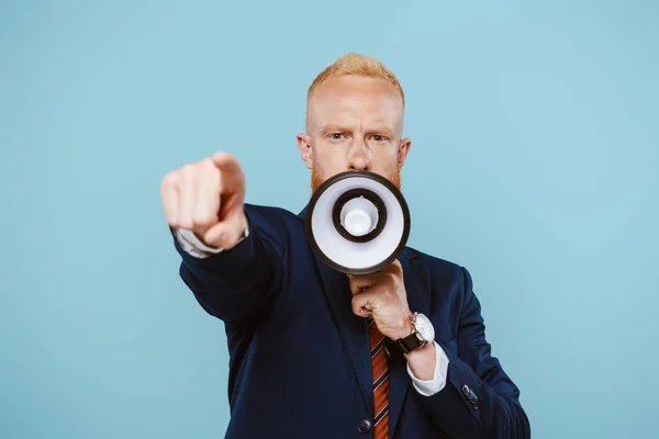 Angry bearded businessman pointing and screaming into megaphone, isolated on blue — Stock Photo