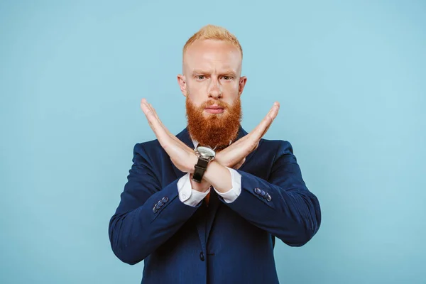 Серйозний бородатий бізнесмен у костюмі, який не показує жодного знаку, ізольований на синьому — стокове фото