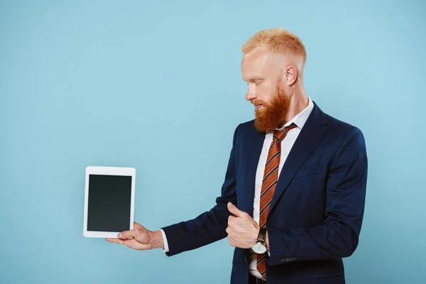 Hombre de negocios barbudo en traje mostrando tableta digital con pantalla en blanco, aislado en azul - foto de stock