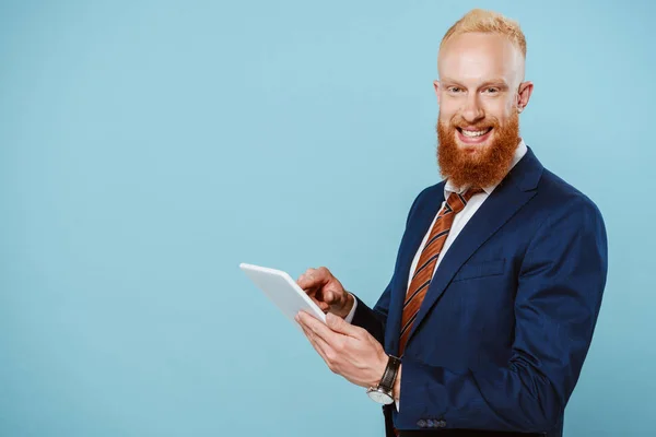 Heureux homme d'affaires barbu en costume à l'aide d'une tablette numérique, isolé sur bleu — Photo de stock