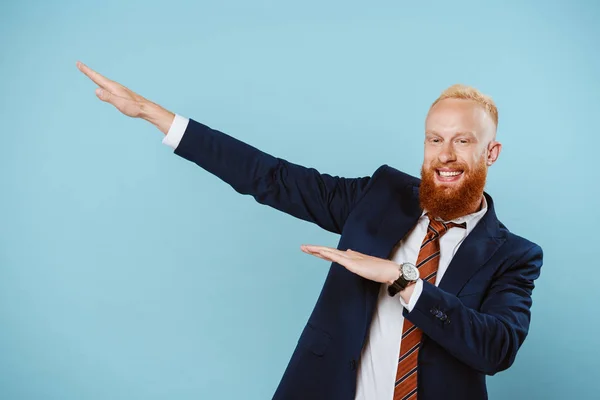 Cheerful bearded businessman in suit gesturing isolated on blue — Stock Photo