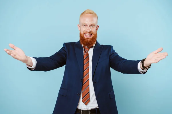 Alegre hombre de negocios barbudo en traje con los brazos abiertos, aislado en azul - foto de stock