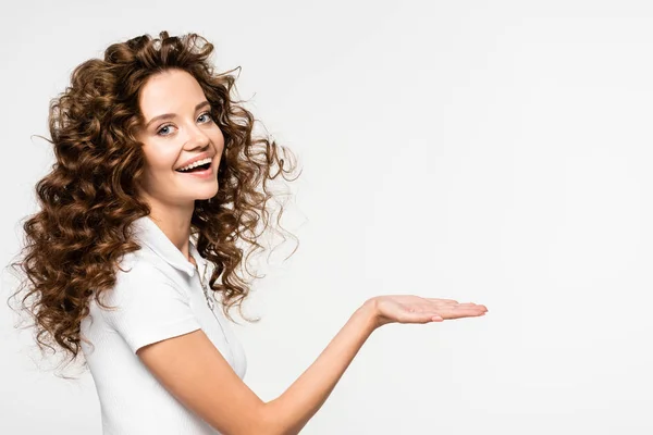 Cheerful curly girl in white t-shirt presenting something, isolated on white — Stock Photo