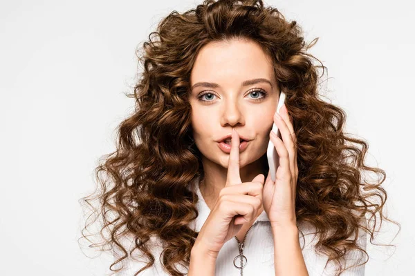 Curly girl talking on smartphone and showing silence symbol, isolated on white — Stock Photo