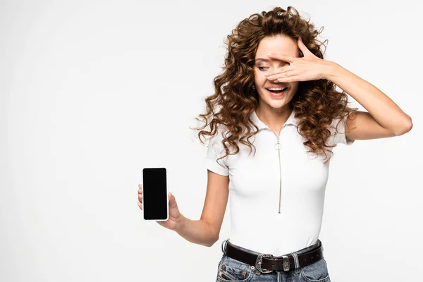 Красивая кудрявая девушка показывает смартфон с пустым экраном, изолированный на белом — стоковое фото