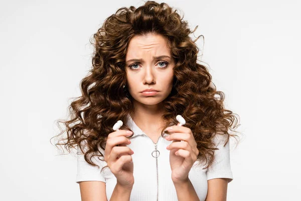 Bela menina triste segurando fones de ouvido sem fio, isolado em branco — Fotografia de Stock