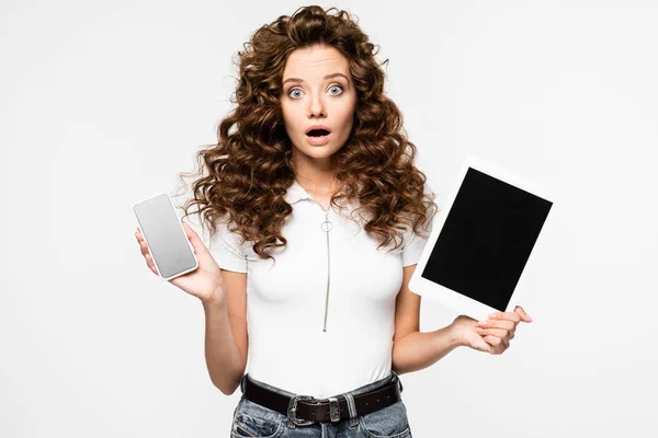 Шокированная женщина показывает смартфон и цифровой планшет, изолированный на белом — стоковое фото
