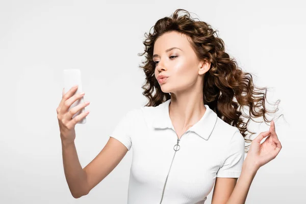 Привлекательная кудрявая девушка делает селфи на смартфоне, изолированная на белом — стоковое фото