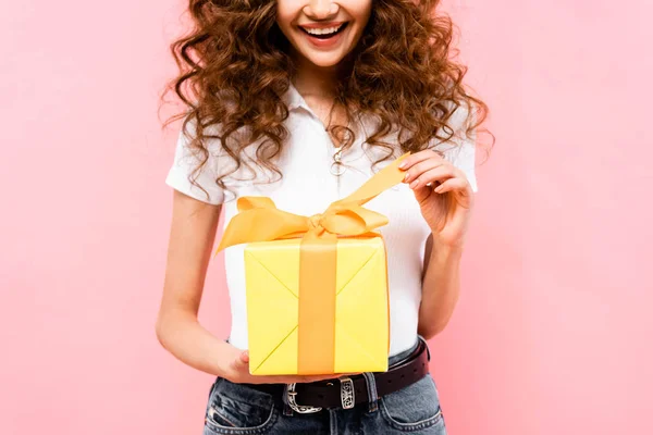 Vue recadrée de heureuse fille bouclée tenant boîte cadeau, isolé sur rose — Photo de stock