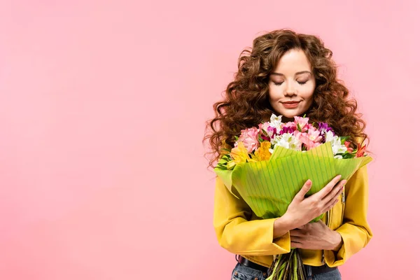 Felice ragazza riccia con gli occhi chiusi in possesso di mazzo di fiori, isolato su rosa — Foto stock