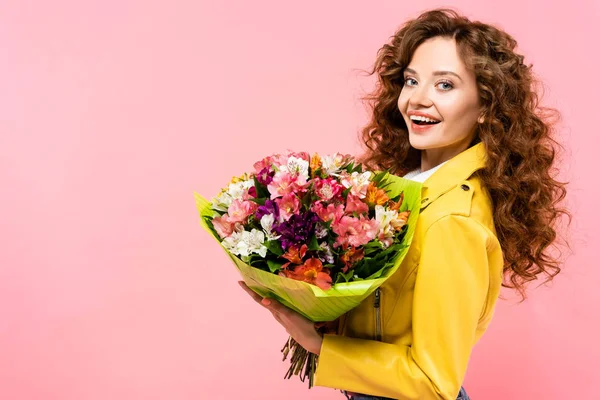 Allegra ragazza riccia in possesso di mazzo di fiori, isolato su rosa — Foto stock