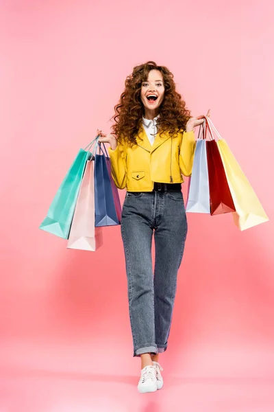 Excitada chica rizada sosteniendo bolsas de compras, aislado en rosa - foto de stock