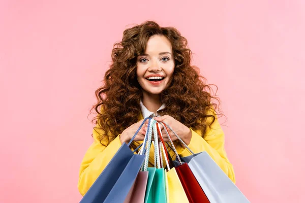 Hermosa chica rizada sosteniendo bolsas de compras, aislado en rosa - foto de stock