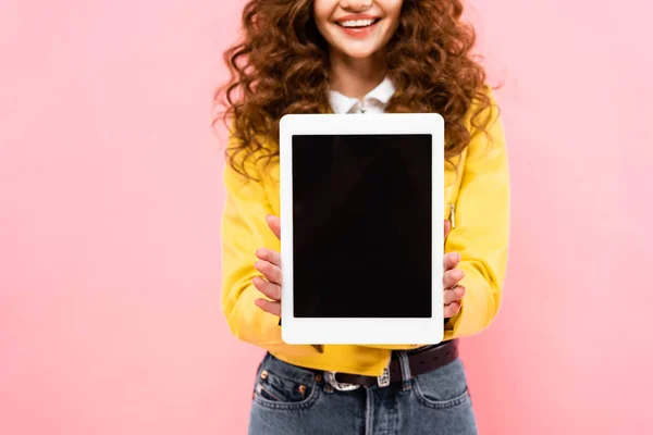 Recortado vista de rizado sonriente chica mostrando tableta digital con pantalla en blanco, aislado en rosa - foto de stock