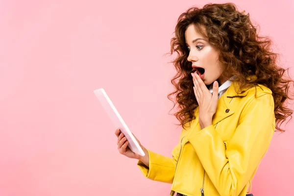 Belle fille choquée à l'aide d'une tablette numérique, isolé sur rose — Photo de stock