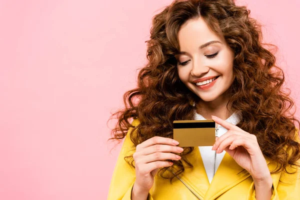 Menina encaracolado sorridente segurando cartão de crédito, isolado em rosa — Fotografia de Stock