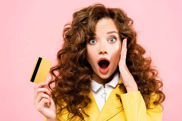 Beautiful shocked girl holding credit card, isolated on pink — Stock Photo