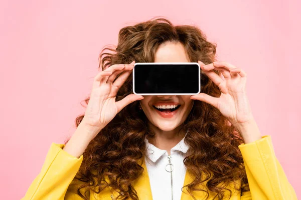 Lächelndes Mädchen, Smartphone mit leerem Bildschirm vor dem Gesicht, isoliert auf rosa — Stockfoto