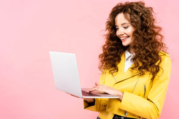 Happy curly woman using laptop, isolated on pink — Stock Photo