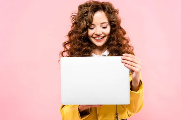 Smiling curly woman using laptop, isolated on pink — Stock Photo