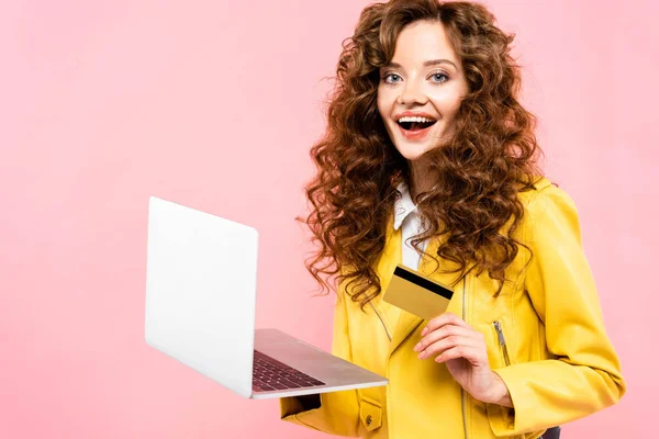 Heureuse bouclée femme shopping en ligne avec carte de crédit et ordinateur portable, isolé sur rose — Photo de stock