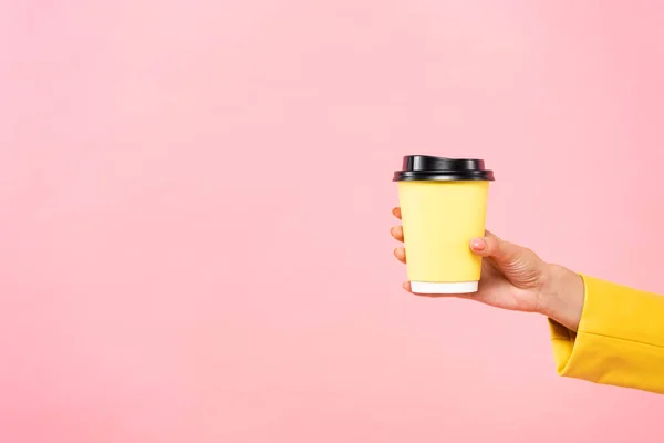 Vista cortada de mulher segurando copo descartável amarelo de café, isolado em rosa — Fotografia de Stock