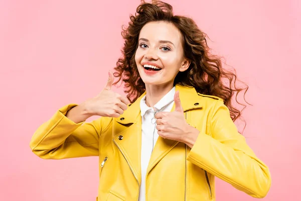 Chica rizada de moda en chaqueta de cuero amarillo que muestra los pulgares hacia arriba, aislado en rosa - foto de stock