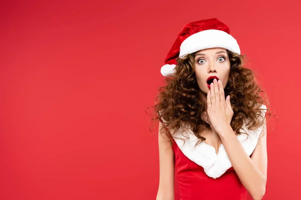 Felice ragazza sorpresa gesticolando in costume da Babbo Natale, isolato sul rosso — Foto stock