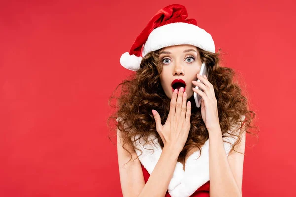 Mujer sorprendida en traje de santa hablando en el teléfono inteligente, aislado en rojo - foto de stock