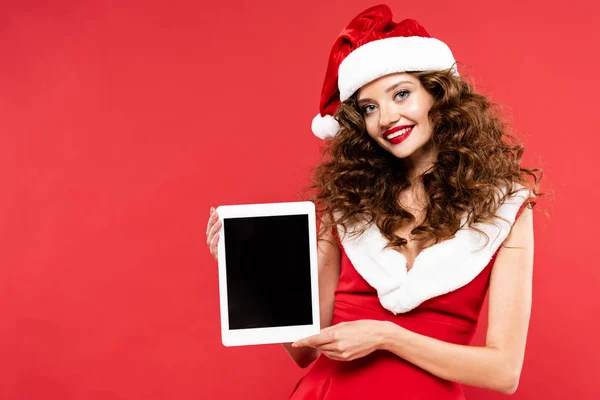 Красива дівчина в костюмі Санти, що показує цифровий планшет з порожнім екраном, ізольована на червоному — стокове фото