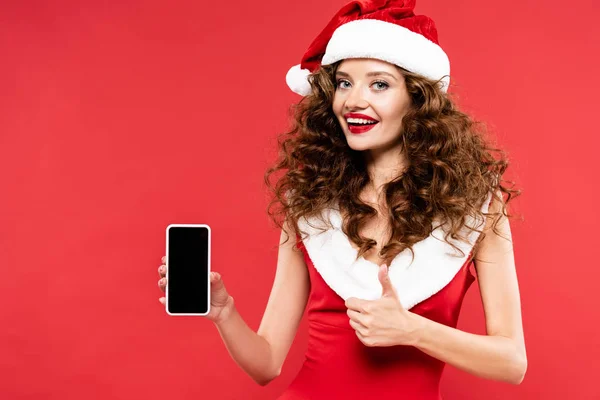 Femme heureuse en costume de Père Noël montrant smartphone et pouce levé, isolé sur rouge — Photo de stock
