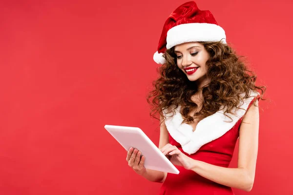 Smiling girl in santa costume using digital tablet, isolated on red — Stock Photo