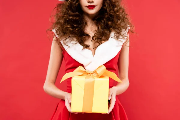 Recortado vista de chica en traje de santa celebración de regalo de Navidad, aislado en rojo - foto de stock