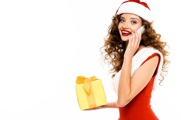 Attraente ragazza in costume da Babbo Natale in possesso di regalo di Natale e parlando su smartphone, isolato su bianco — Foto stock